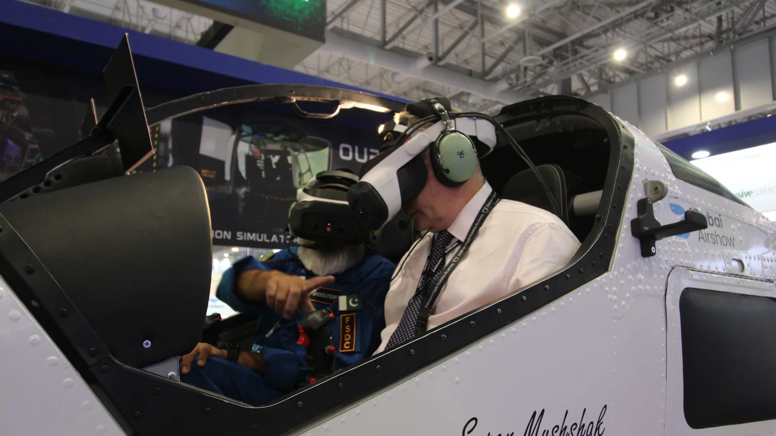A visitor flying the AeroMix Super Mushshak simulator in a Varjo XR-4 headset with an FSDC instructor at Dubai Airshow 2025